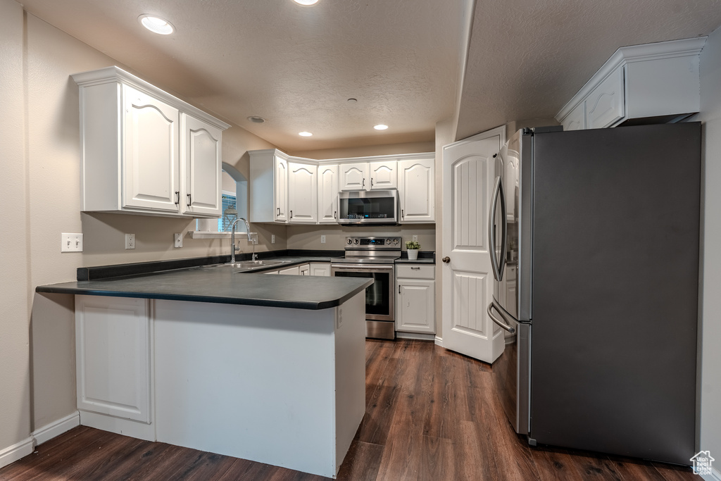 Kitchen with appliances with stainless steel finishes, a sink, a peninsula, dark countertops, and recessed lighting
