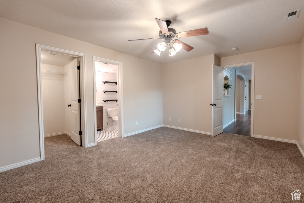 Unfurnished bedroom featuring carpet floors, a walk in closet, baseboards, arched walkways, and a closet