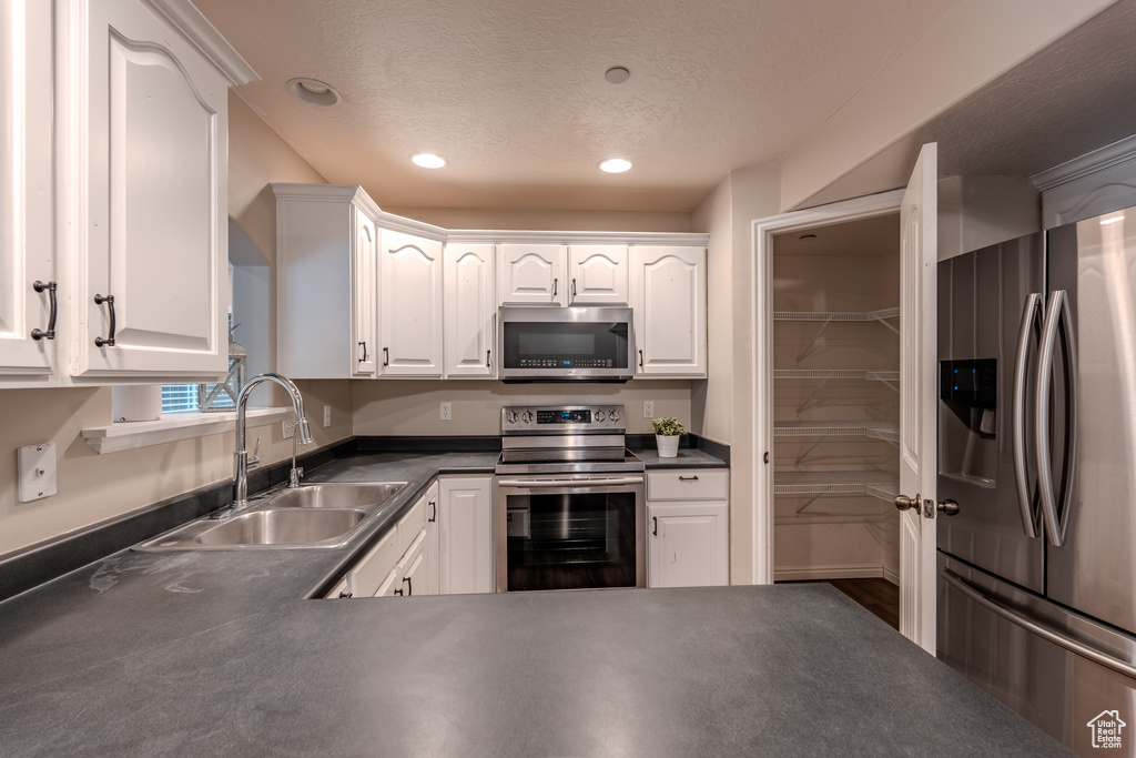 Kitchen with appliances with stainless steel finishes, a sink, dark countertops, white cabinetry, and recessed lighting