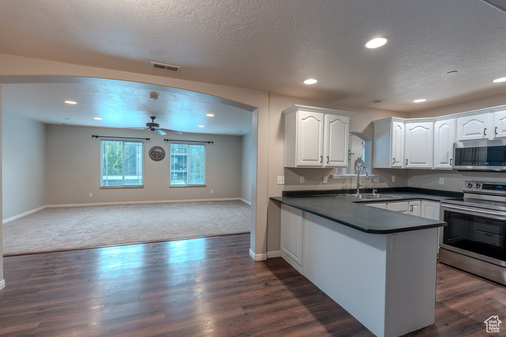 Kitchen with stainless steel appliances, dark countertops, a sink, ceiling fan, and white cabinetry