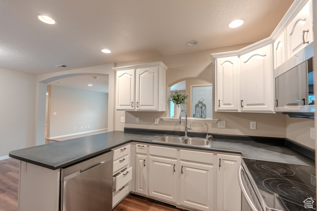 Kitchen with arched walkways, appliances with stainless steel finishes, a sink, dark countertops, and recessed lighting