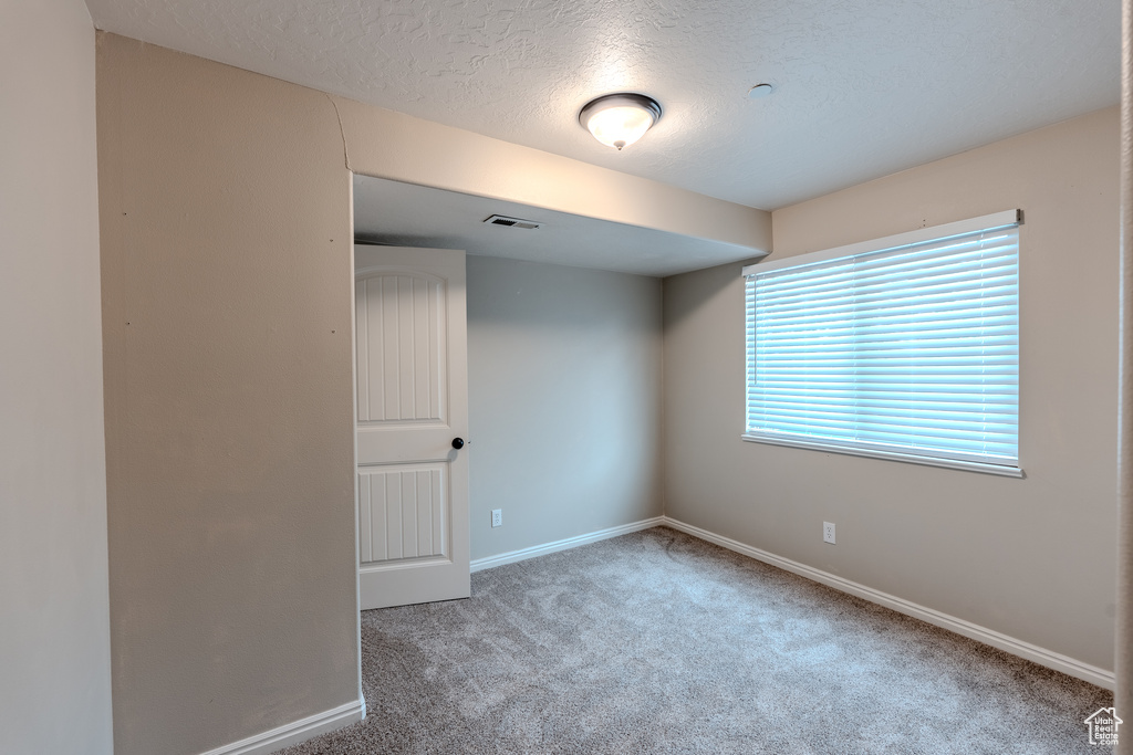 Empty room with carpet flooring, a textured ceiling, and baseboards