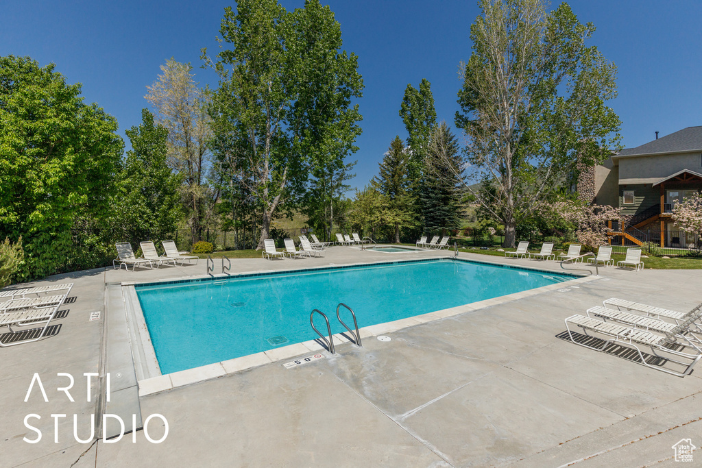 Community pool with a patio area, a community hot tub, and view of wooded area