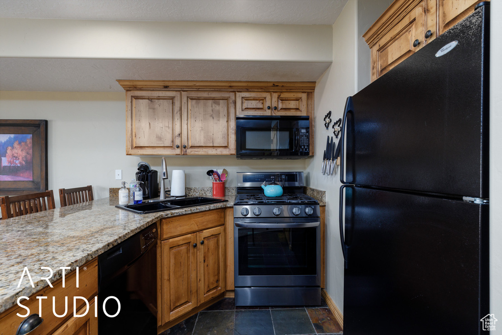 Kitchen featuring black appliances, a sink, light stone countertops, brown cabinetry, and a peninsula