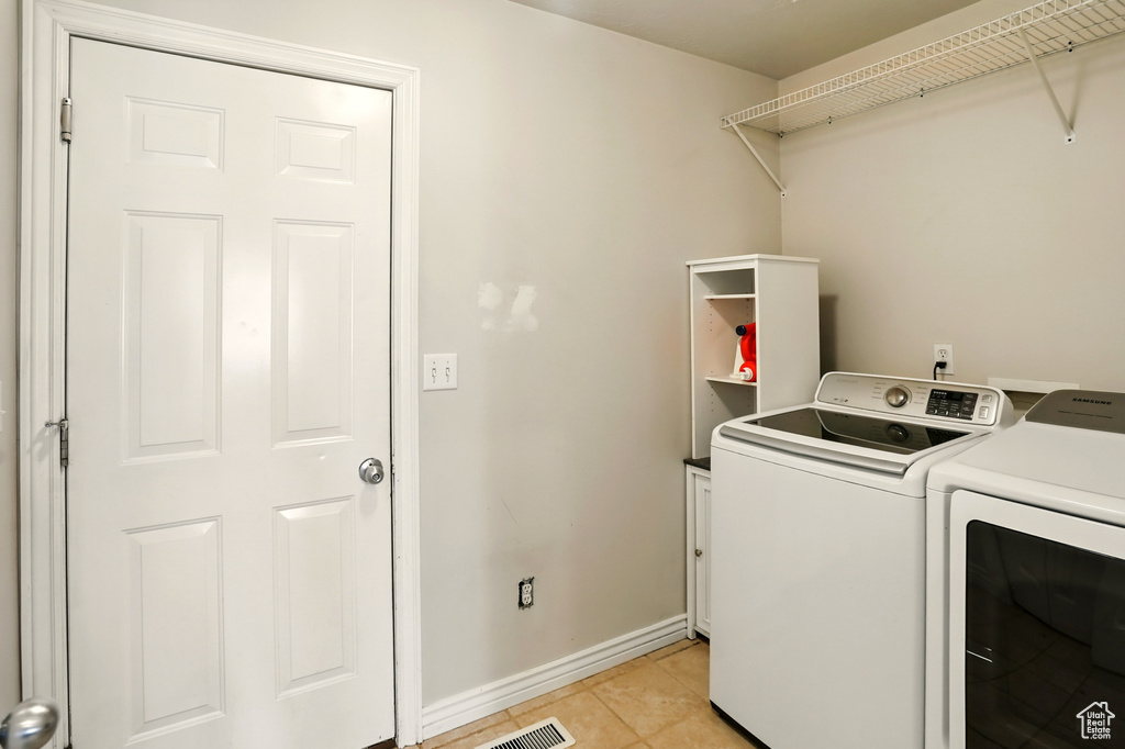 Laundry area featuring separate washer and dryer, light tile patterned flooring, and baseboards