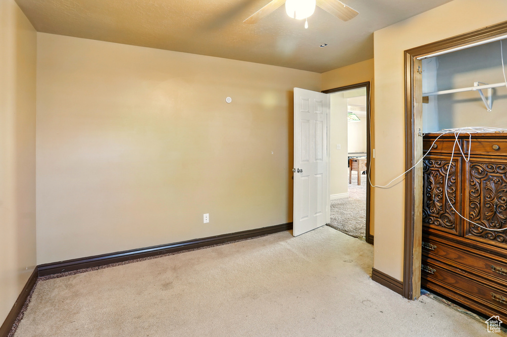 Unfurnished bedroom with light colored carpet, baseboards, and a ceiling fan