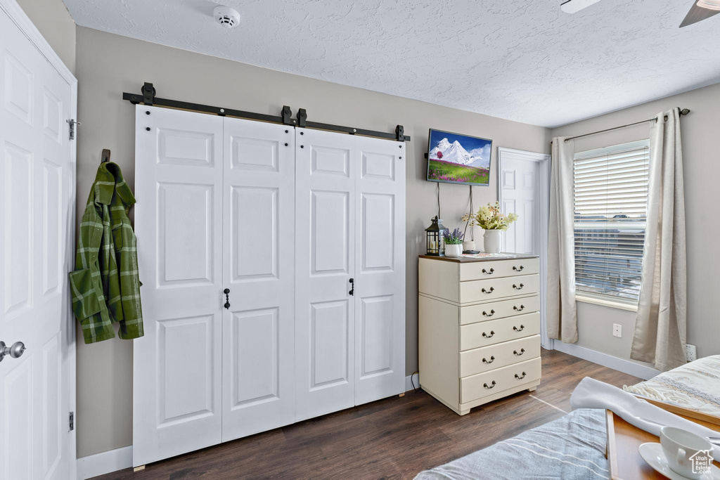 Bedroom featuring a barn door, dark wood-type flooring, a textured ceiling, and baseboards