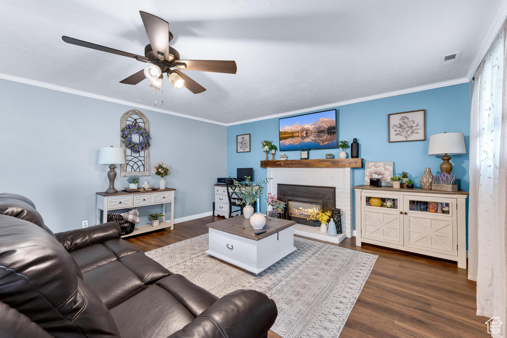 Living area with a ceiling fan, dark wood-type flooring, a fireplace, ornamental molding, and baseboards