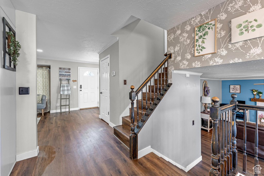 Foyer entrance with wood finished floors, wallpapered walls, baseboards, ornamental molding, and a textured ceiling