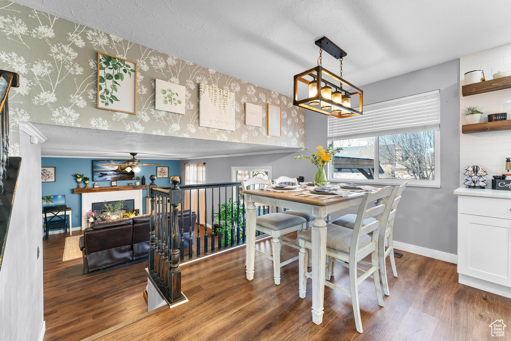 Dining space featuring a ceiling fan, wood finished floors, baseboards, a chandelier, and wallpapered walls