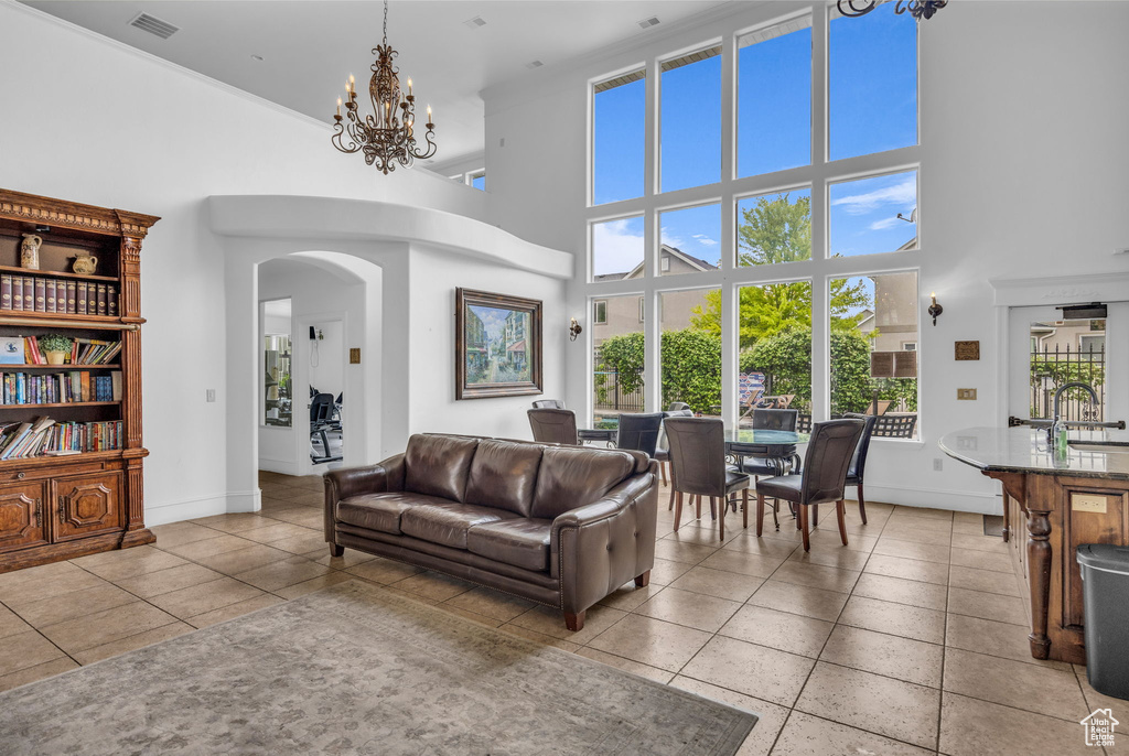 Living area featuring a high ceiling, light tile patterned floors, arched walkways, baseboards, and a chandelier