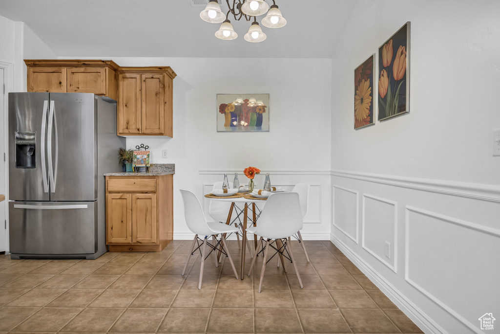 Tiled dining area featuring a chandelier, a wainscoted wall, and a decorative wall