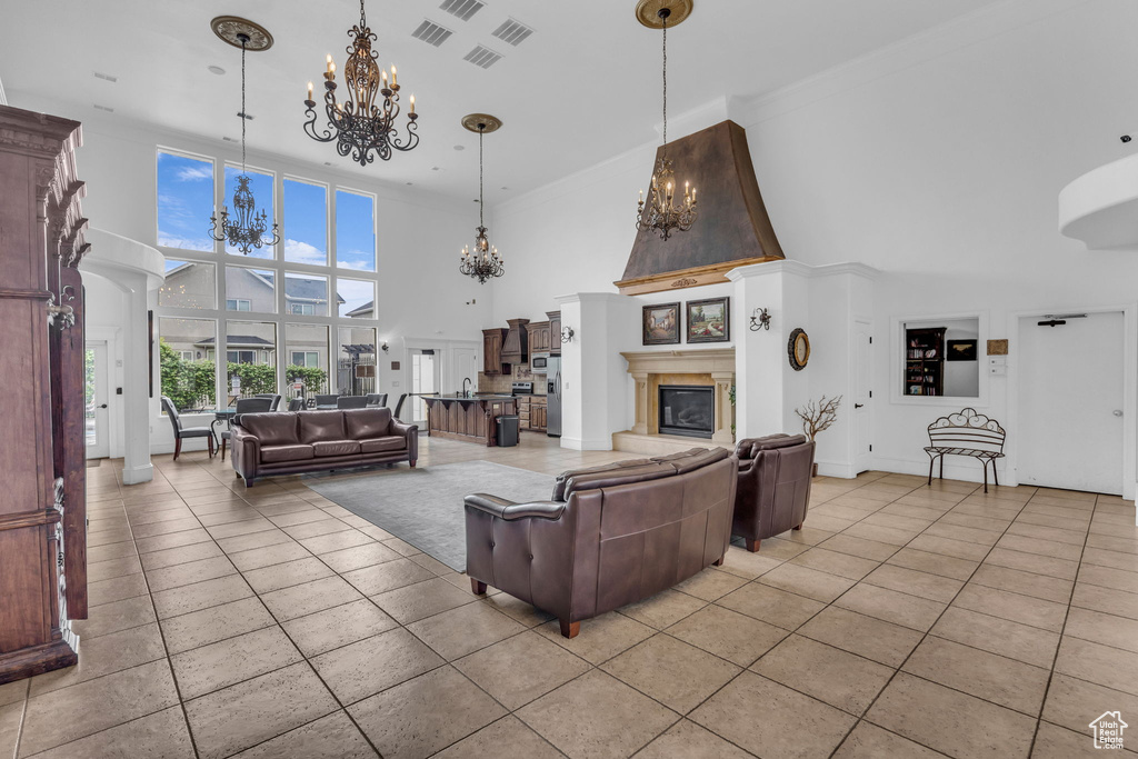 Living area featuring a chandelier, a towering ceiling, light tile patterned flooring, and a glass covered fireplace