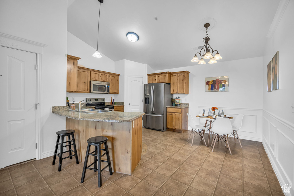 Kitchen featuring stainless steel appliances, a sink, a peninsula, lofted ceiling, and brown cabinetry