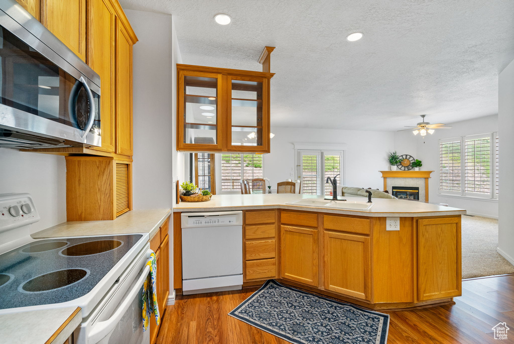 Kitchen with white appliances, a sink, a peninsula, a textured ceiling, and a glass covered fireplace