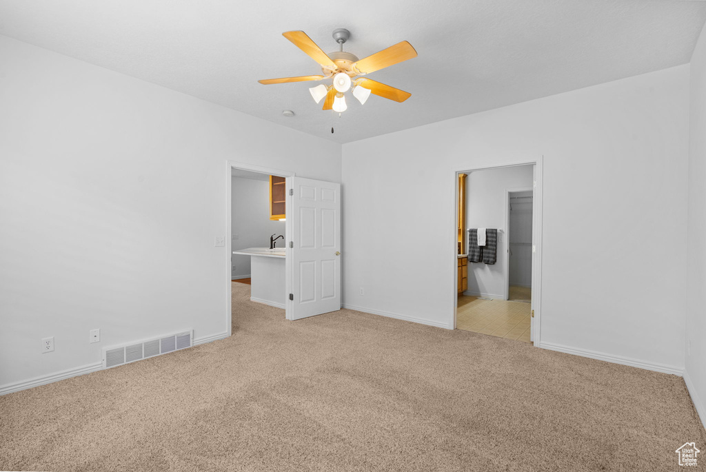 Unfurnished bedroom with carpet floors, baseboards, a walk in closet, a ceiling fan, and a sink