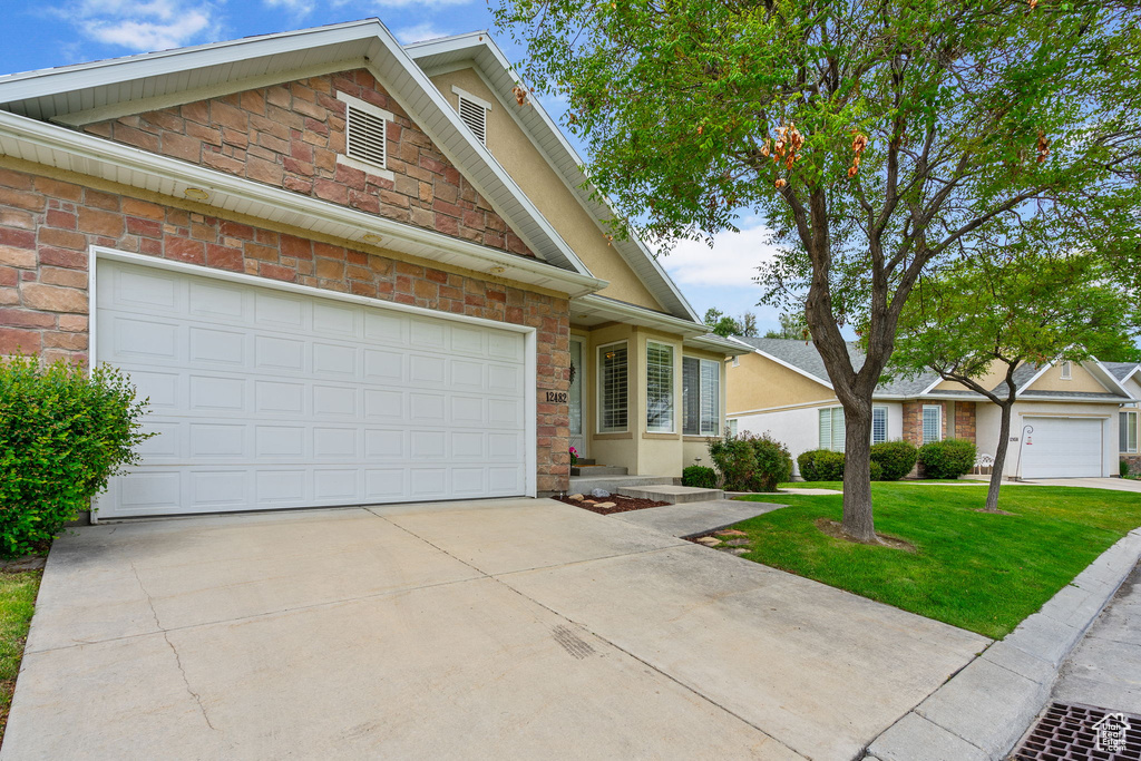 Traditional home with driveway, a front lawn, and stone siding