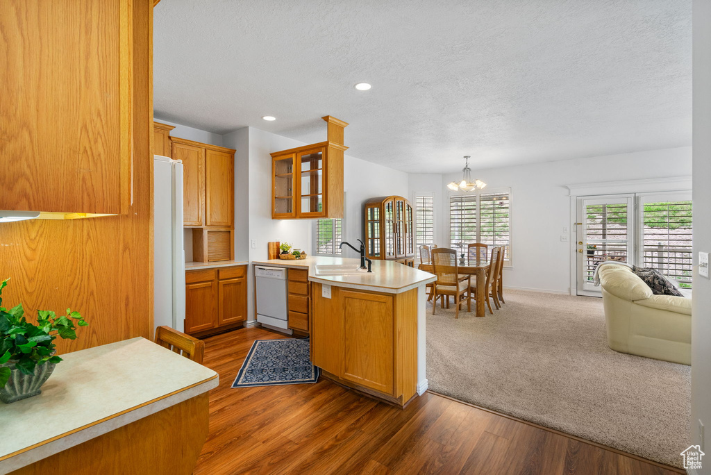Kitchen featuring white appliances, a peninsula, a sink, a textured ceiling, and glass insert cabinets