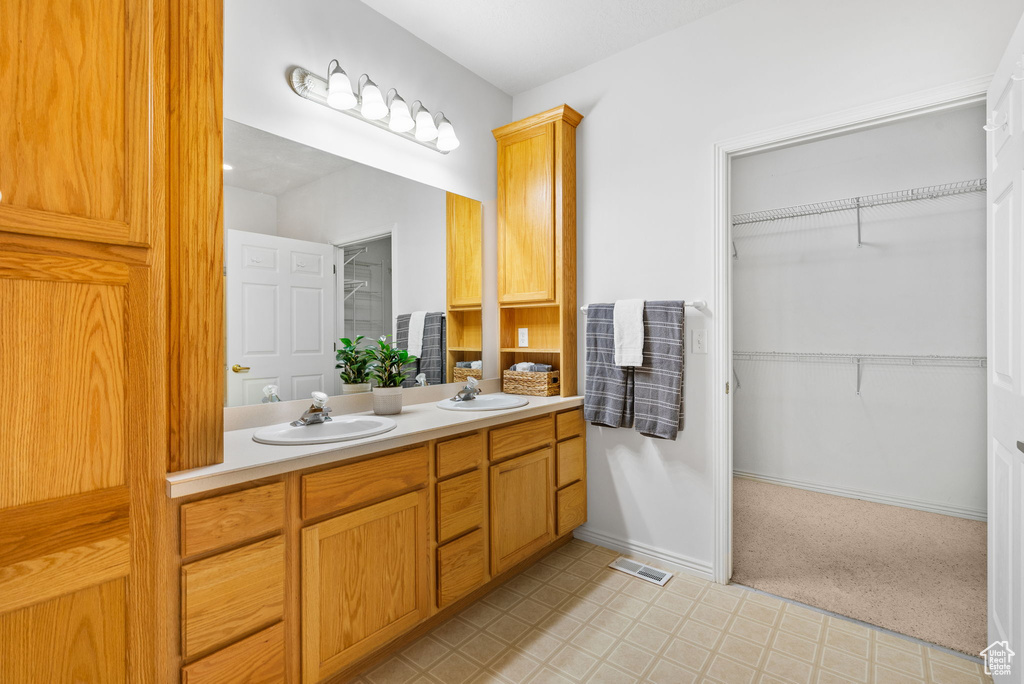 Full bath featuring double vanity, tile patterned floors, a walk in closet, and baseboards