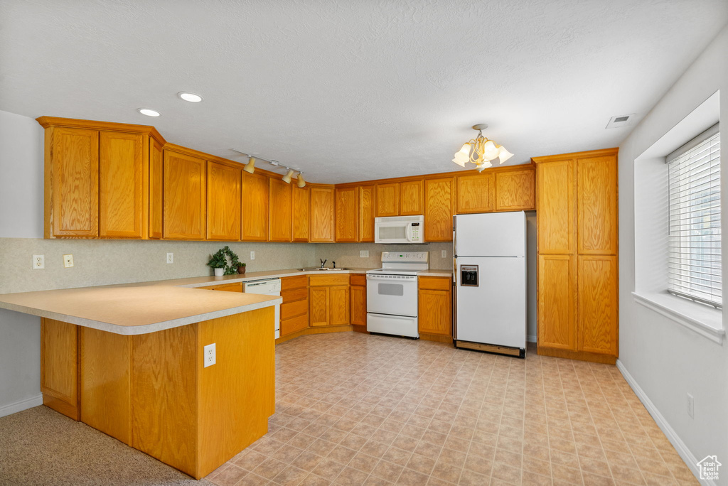 Kitchen featuring white appliances, a peninsula, light countertops, a sink, and brown cabinetry