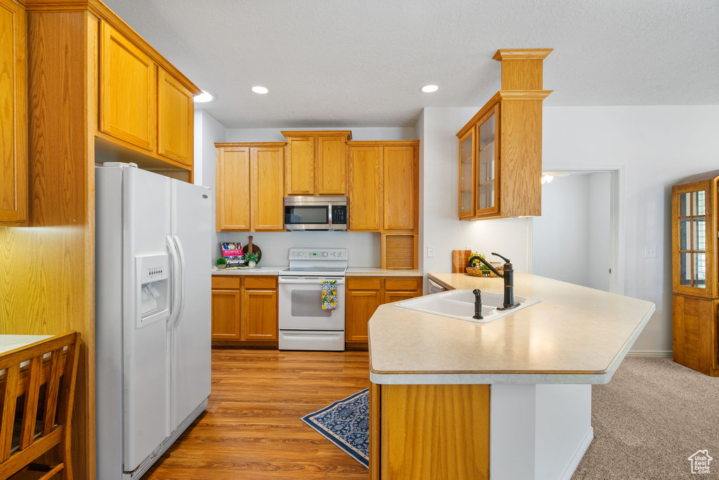 Kitchen with white appliances, a sink, a peninsula, light countertops, and recessed lighting