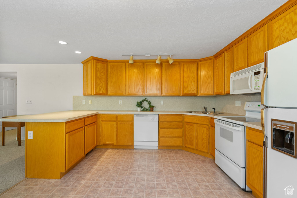 Kitchen featuring white appliances, a peninsula, light countertops, track lighting, and a sink