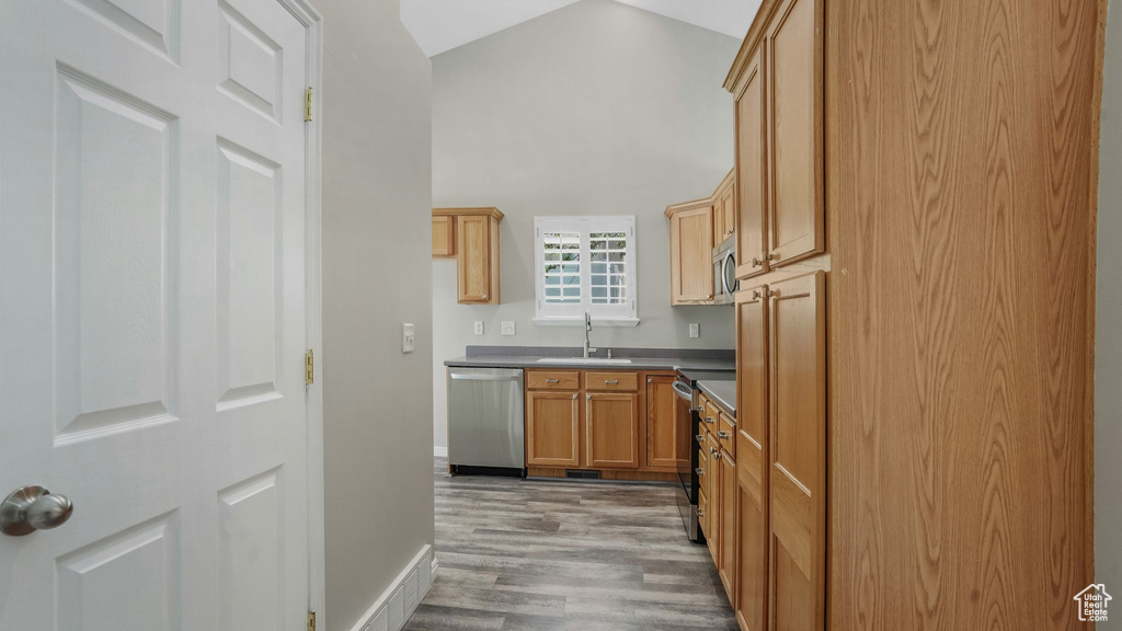 Kitchen with appliances with stainless steel finishes, a sink, light wood-style floors, dark countertops, and baseboards