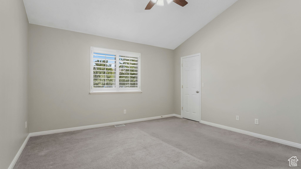 Carpeted empty room featuring ceiling fan, baseboards, and vaulted ceiling