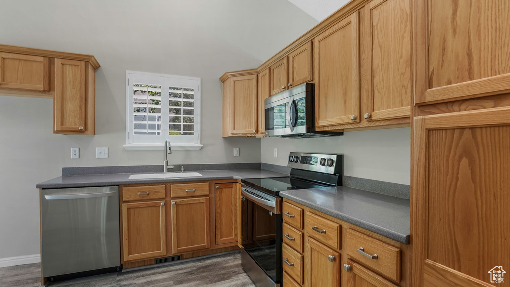Kitchen with appliances with stainless steel finishes, a sink, dark countertops, and dark wood-style floors