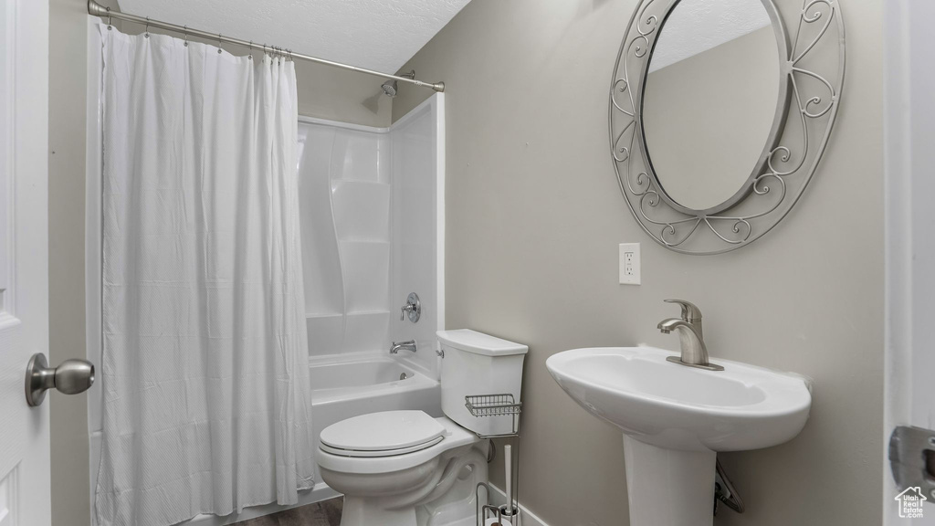Full bath with shower / tub combo, toilet, a textured ceiling, and wood finished floors