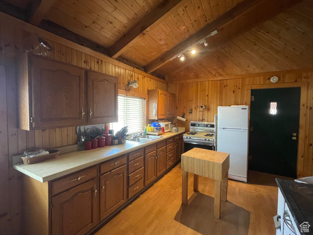 Kitchen featuring freestanding refrigerator, wood walls, gas range, light wood-style floors, and light countertops