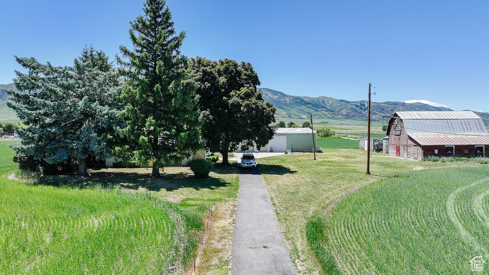 View of grassy yard with an outdoor structure, driveway, a barn, and a mountain view