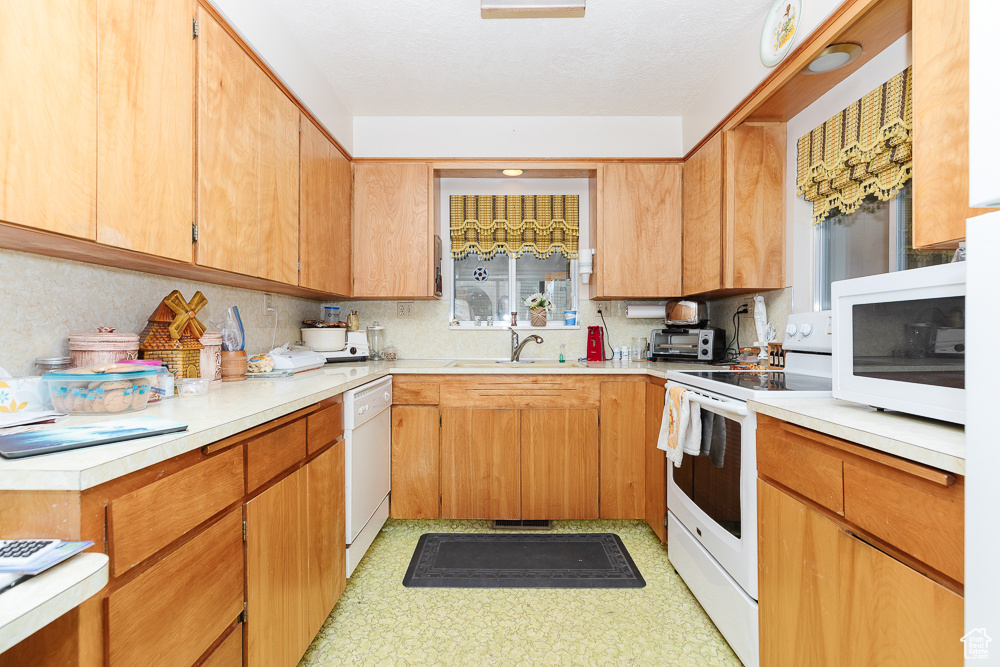Kitchen with white appliances, a sink, decorative backsplash, and light countertops