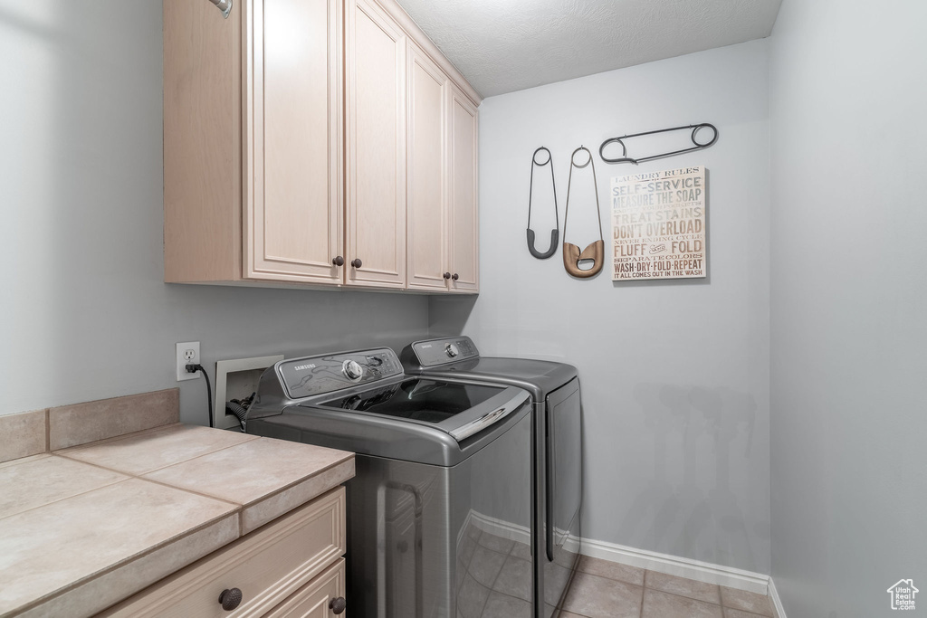 Washroom featuring cabinet space, washing machine and dryer, light tile patterned floors, and baseboards