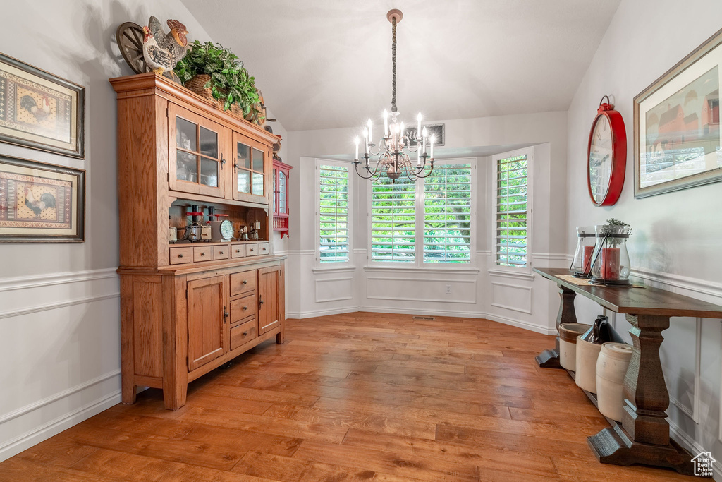 Dining room featuring a chandelier, a decorative wall, light wood-type flooring, a wainscoted wall, and lofted ceiling