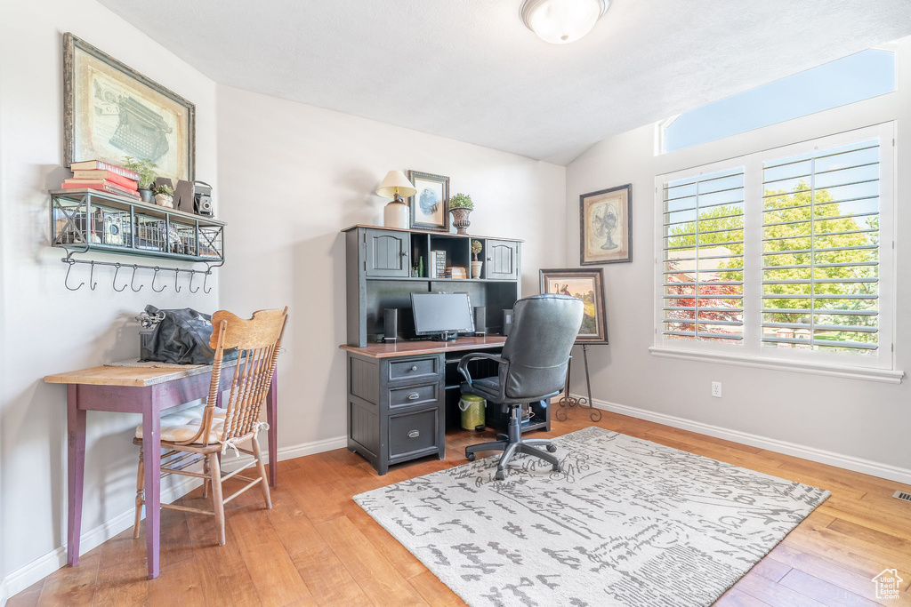 Office area with light wood finished floors, lofted ceiling, and baseboards