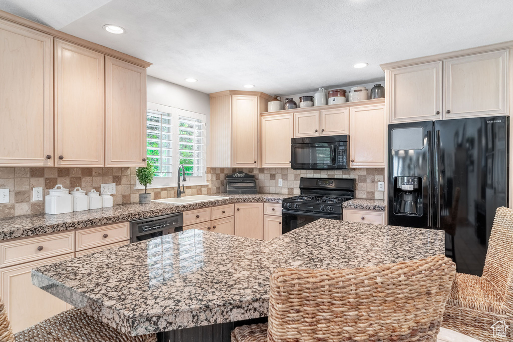 Kitchen featuring black appliances, a sink, a kitchen island, tasteful backsplash, and recessed lighting