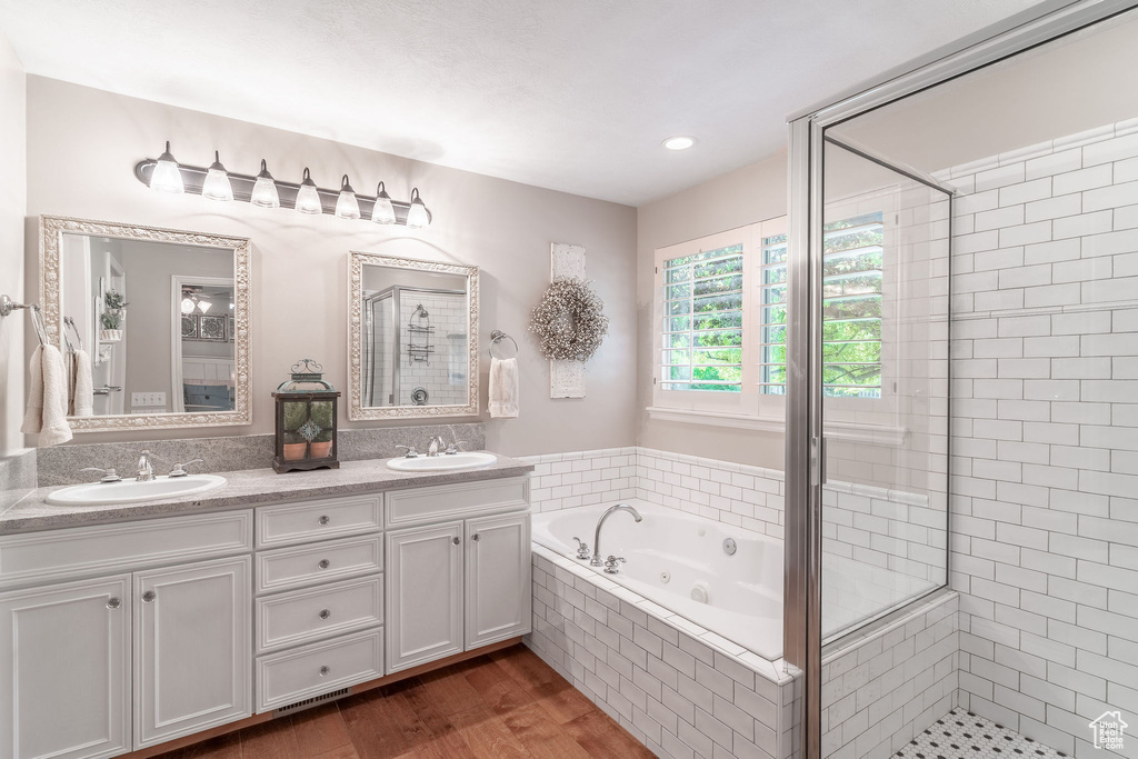 Full bath with a stall shower, a whirlpool tub, double vanity, and wood finished floors