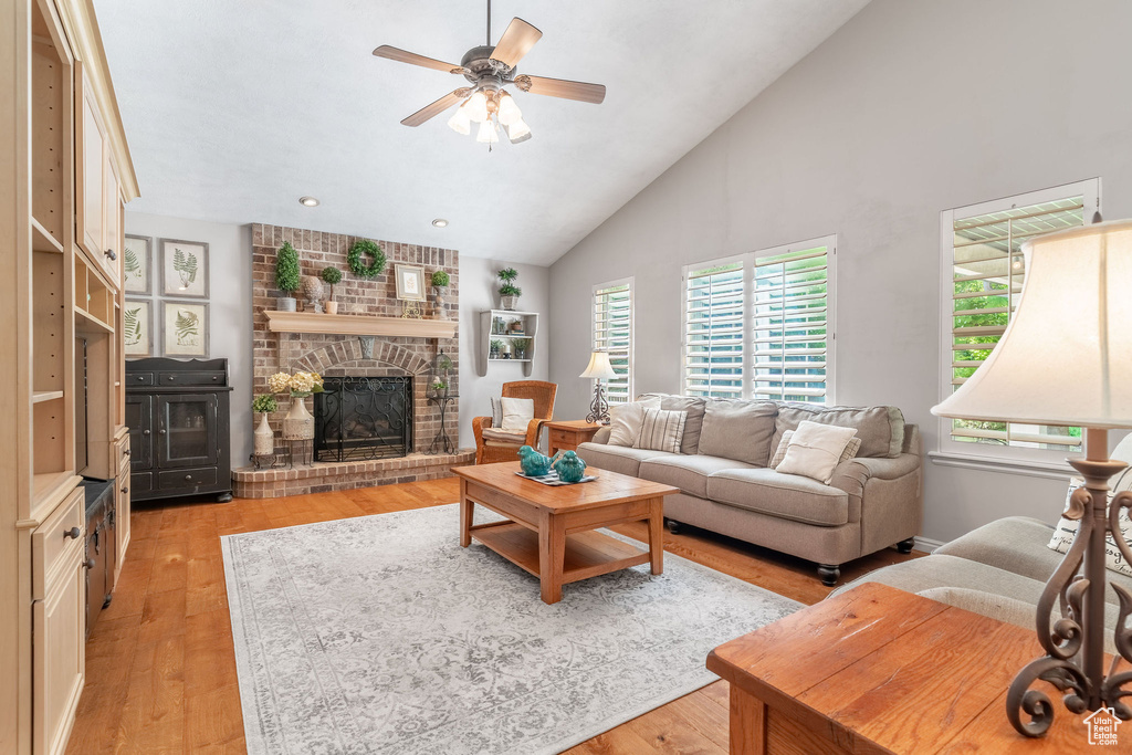 Living area with light wood-style flooring, ceiling fan, a fireplace, high vaulted ceiling, and recessed lighting