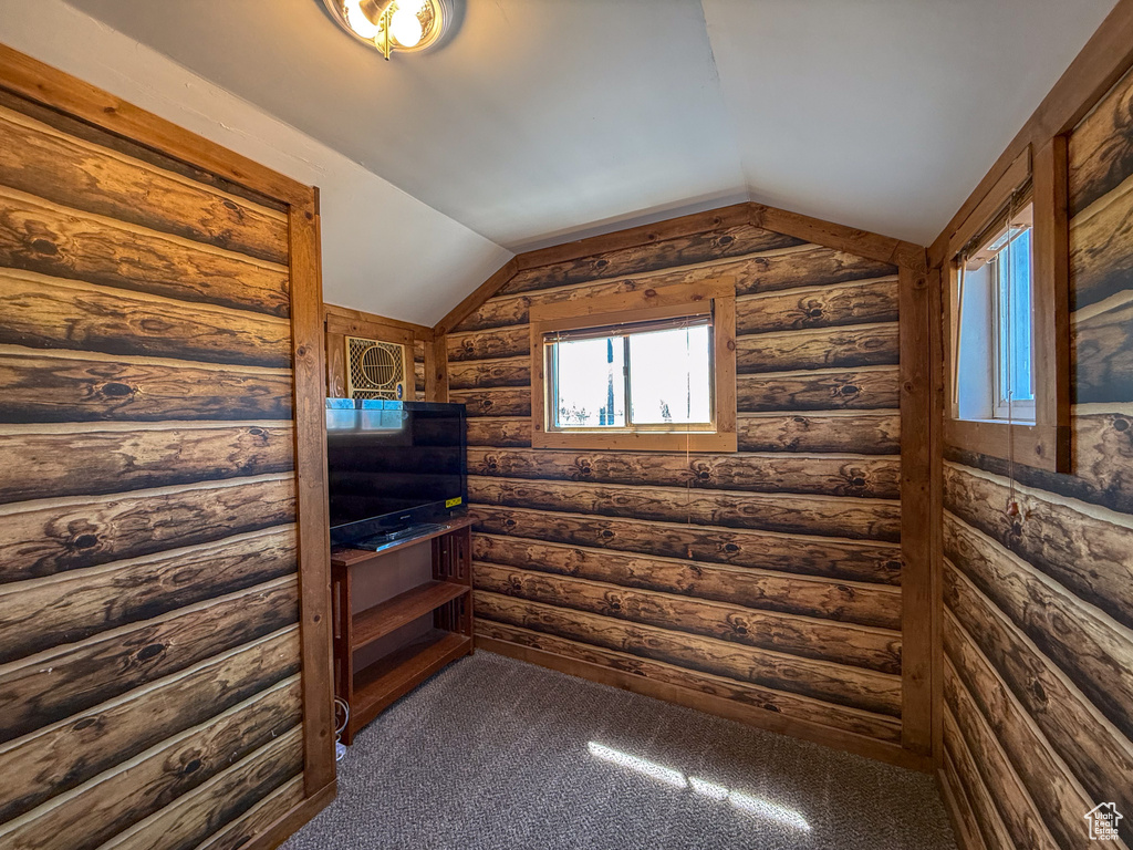 Spare room featuring vaulted ceiling, rustic walls, and dark colored carpet