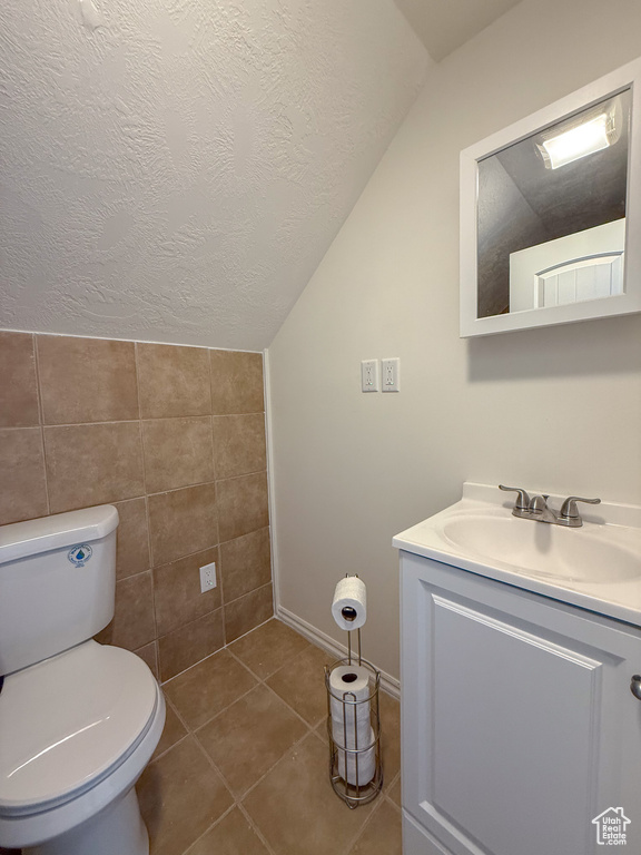 Half bath with lofted ceiling, vanity, toilet, a textured ceiling, and tile walls
