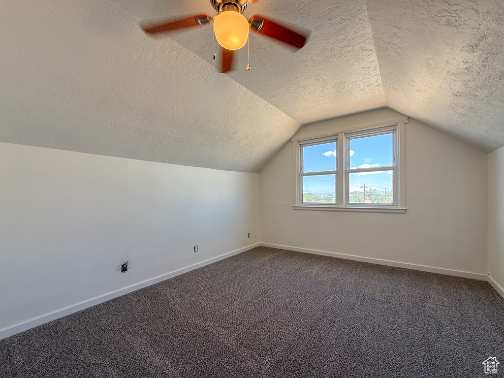 Additional living space with a textured ceiling, baseboards, dark colored carpet, vaulted ceiling, and a ceiling fan