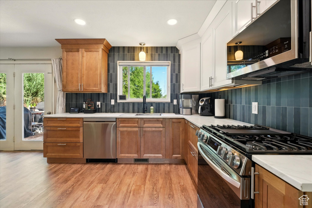 Kitchen with appliances with stainless steel finishes, a sink, light countertops, backsplash, and light wood-type flooring