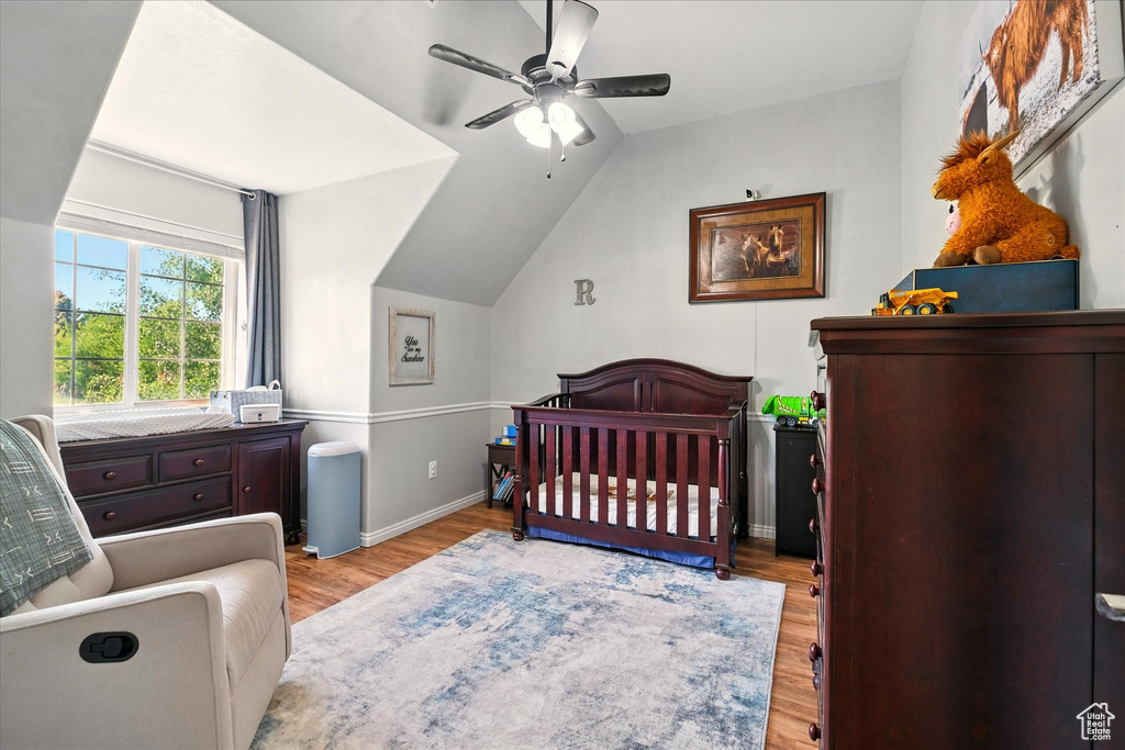 Bedroom featuring wood finished floors, a nursery area, lofted ceiling, a ceiling fan, and baseboards