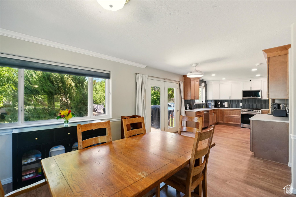 Dining room with ornamental molding, light wood finished floors, recessed lighting, and french doors