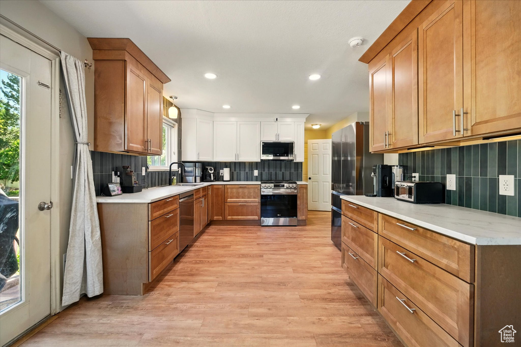 Kitchen with appliances with stainless steel finishes, tasteful backsplash, light wood finished floors, recessed lighting, and light countertops