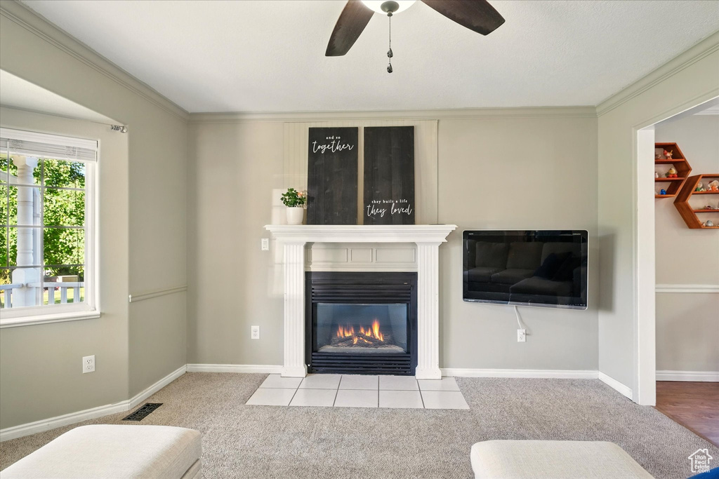 Carpeted living area featuring a fireplace, ceiling fan, ornamental molding, and baseboards