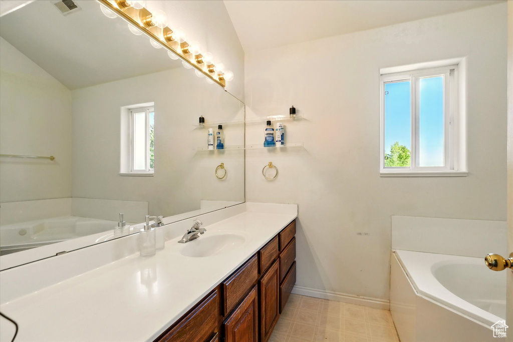 Full bathroom featuring vanity, a bath, baseboards, lofted ceiling, and tile patterned floors