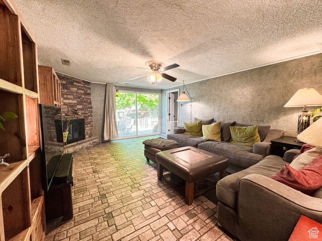 Living area featuring ceiling fan, brick patterned flooring, and a stone fireplace