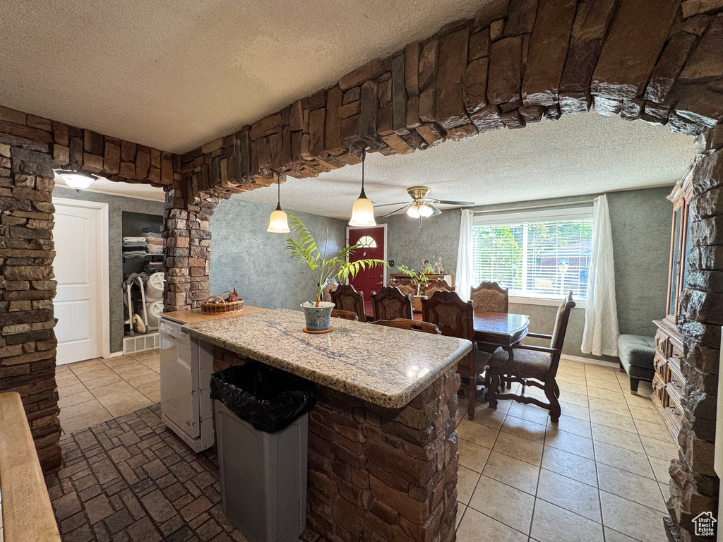 Kitchen featuring a textured ceiling, a kitchen island, pendant lighting, a ceiling fan, and tile patterned flooring